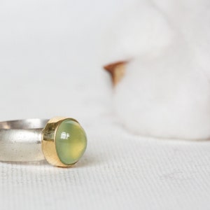 May include: A silver and gold ring with a green gemstone. The ring is set on a white background.