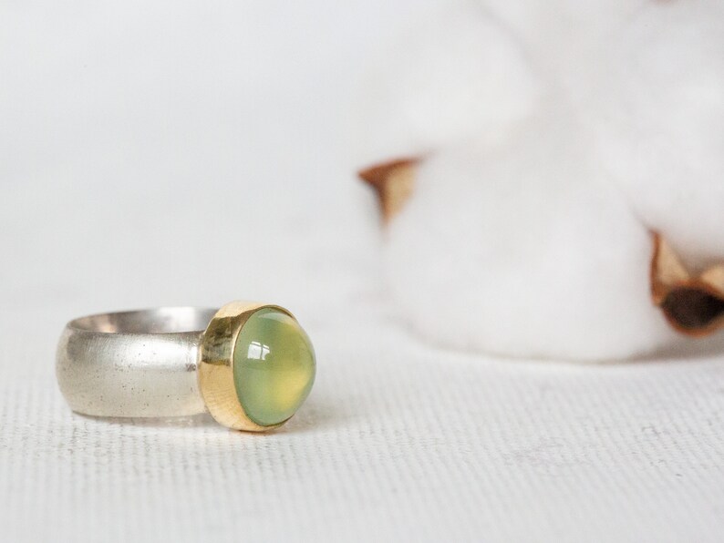 May include: A silver and gold ring with a green gemstone. The ring is set on a white background.