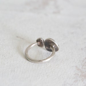 Puede incluir: Un anillo de plata con una piedra redonda y plana engastada en el centro. El anillo est&aacute; abierto por un lado y tiene un dise&ntilde;o simple y minimalista.