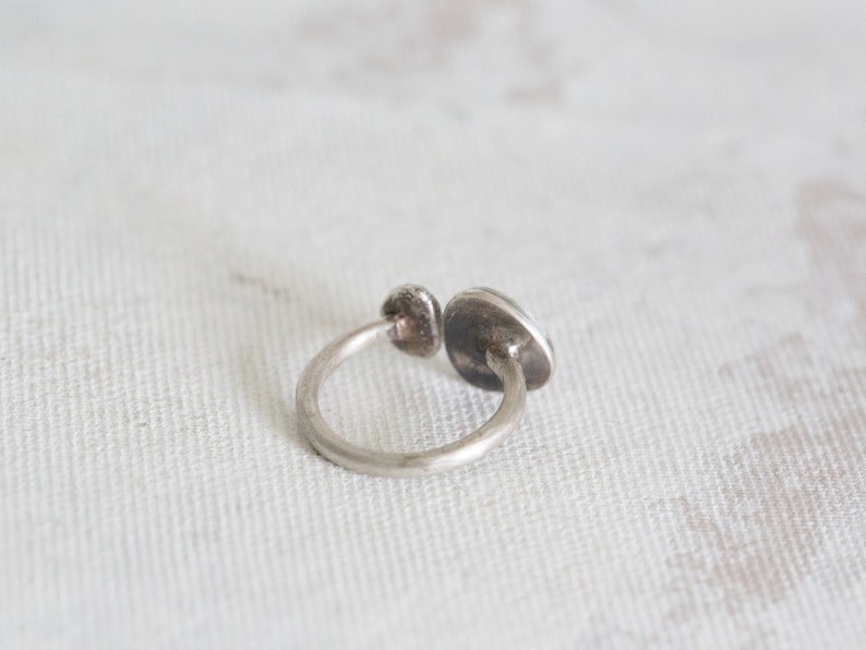 Puede incluir: Un anillo de plata con una piedra redonda y plana engastada en el centro. El anillo est&aacute; abierto por un lado y tiene un dise&ntilde;o simple y minimalista.