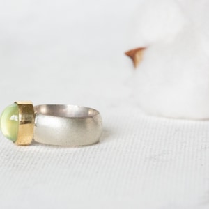 May include: A silver and gold ring with a green gemstone. The ring is set on a white background.