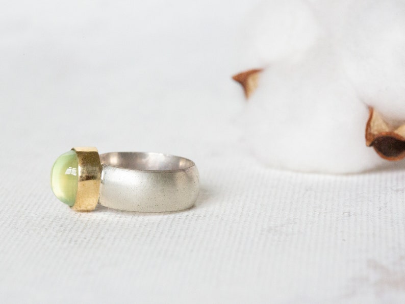 May include: A silver and gold ring with a green gemstone. The ring is set on a white background.