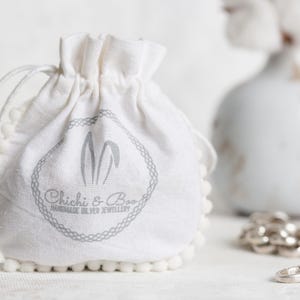 May include: A white cotton drawstring bag with a pom-pom trim. The bag has a gray logo that says "Chichi & Boo Handmade Silver Jewellery".