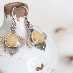 May include: A pair of silver earrings with a yellow gemstone set in a flower-shaped design.
