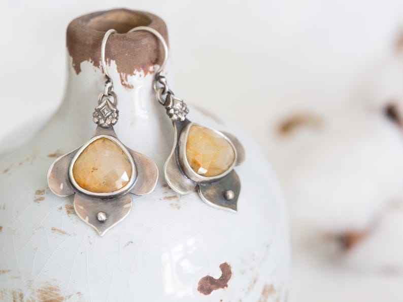 May include: A pair of silver earrings with a yellow gemstone set in a flower-shaped design.