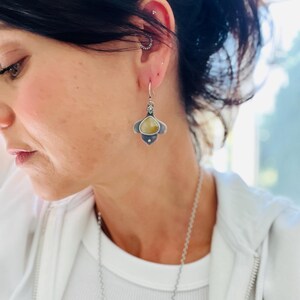 May include: Silver dangle earrings with a teardrop-shaped yellow stone set in a silver flower design.