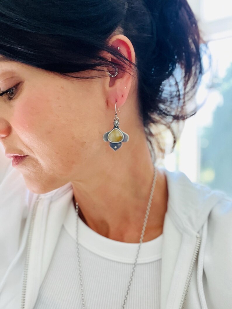 May include: Silver dangle earrings with a teardrop-shaped yellow stone set in a silver flower design.