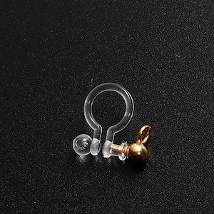 May include: A clear plastic earring back with a gold-colored ball on the end.
