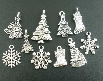 May include: A collection of silver-toned Christmas charms, including detailed Christmas trees, snowflakes, and stockings. These small, decorative pendants are designed for jewelry making or holiday crafts. The charms are displayed against a dark background.