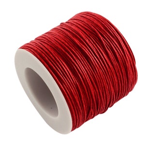 May include: A spool of bright red waxed cord. The cord is tightly wound around a white core, creating a compact, cylindrical shape. The vibrant red color of the cord is eye-catching, suitable for various crafting projects.