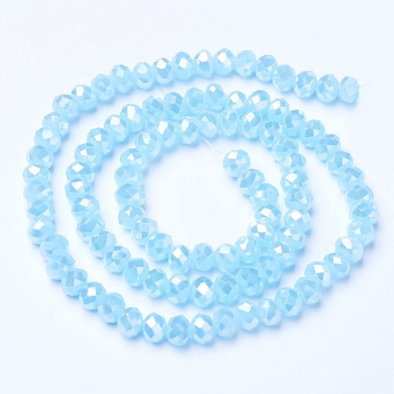 Pu&ograve; includere: Una collana di perline di vetro sfaccettate di colore azzurro chiaro. Le perline sono piccole e rotonde, e hanno un leggero effetto iridescente.