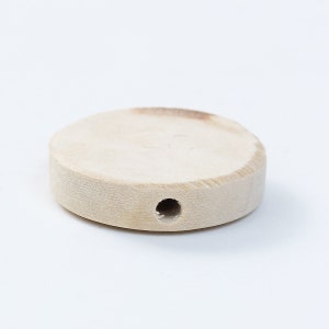 May include: A round, unfinished wooden disc with a hole in the center. The disc is light brown in color and has a smooth surface.