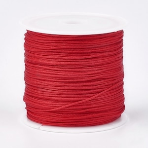 May include: A spool of red cord, wound tightly on a white plastic bobbin.