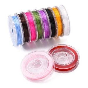 May include: Spools of colorful elastic cord in various colors, including blue, brown, pink, green, purple, black, yellow, and white. Two additional spools of pink and red cord are in the foreground. Ideal for jewelry making and crafts.