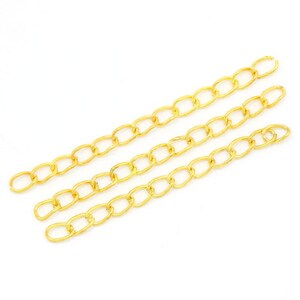 May include: Four strands of gold chain, each with oval links. The chains are laid out in parallel lines on a white background.