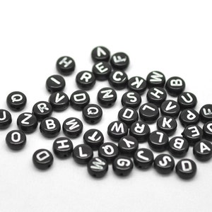 May include: A collection of black round beads with white letters on them. The letters are all different and represent the alphabet.
