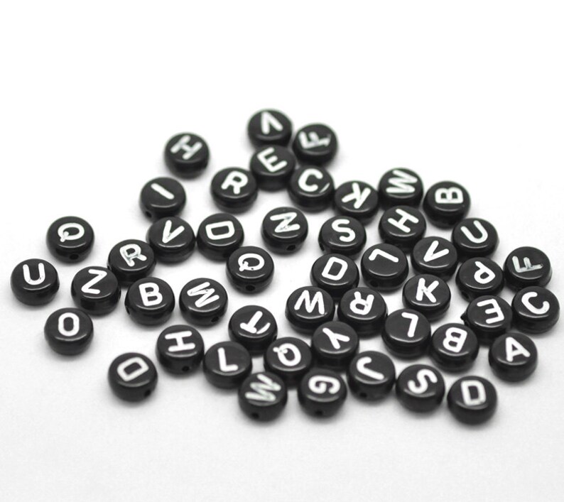 May include: A collection of black round beads with white letters on them. The letters are all different and represent the alphabet.