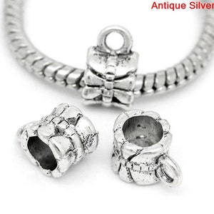 May include: Three antique silver charm beads with a bow design. The beads are designed to be used on a charm bracelet.