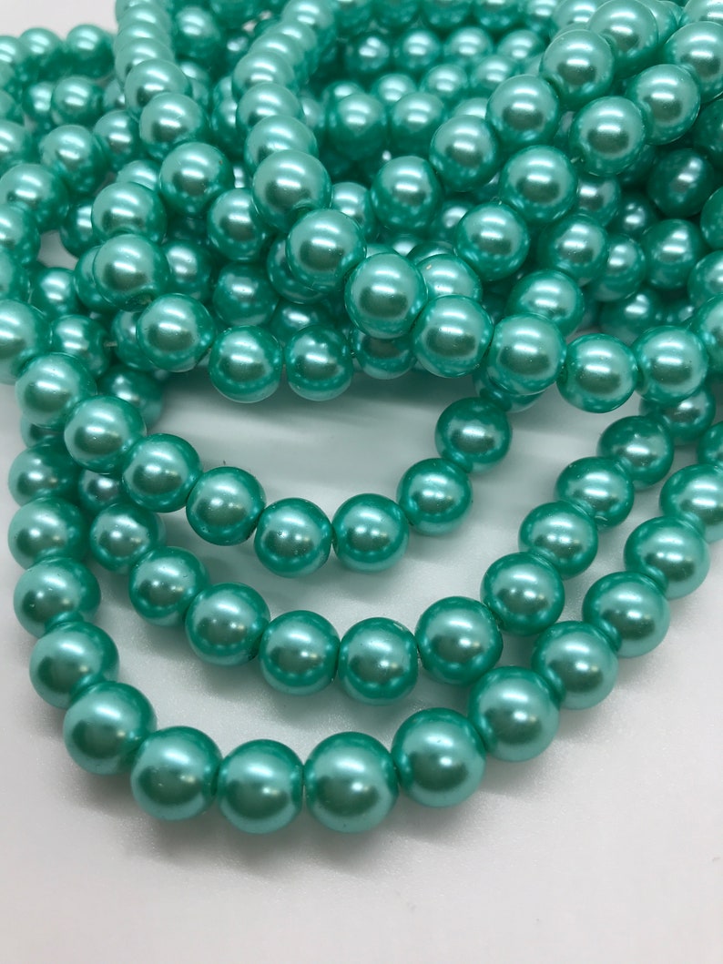 May include: A strand of teal green pearl beads. The beads are round and have a smooth, glossy finish.