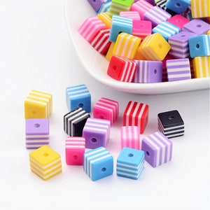 May include: Assortment of colorful striped cube beads with a hole in the center. The beads are made of plastic and are perfect for crafting projects.