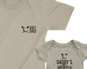 May include: A set of two shirts, one for an adult and one for a baby. The adult shirt is a light gray t-shirt with the text "GOLF DAD" and a golf club and ball graphic. The baby shirt is a light gray bodysuit with the text "DADDY'S golfing BUDDY" and a golf club and ball graphic.