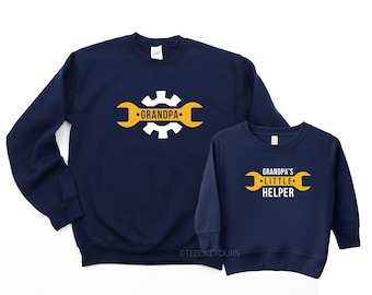 May include: Matching navy blue sweatshirts with a white gear and wrench design. The larger sweatshirt says "Grandpa" and the smaller sweatshirt says "Grandpa's Little Helper".