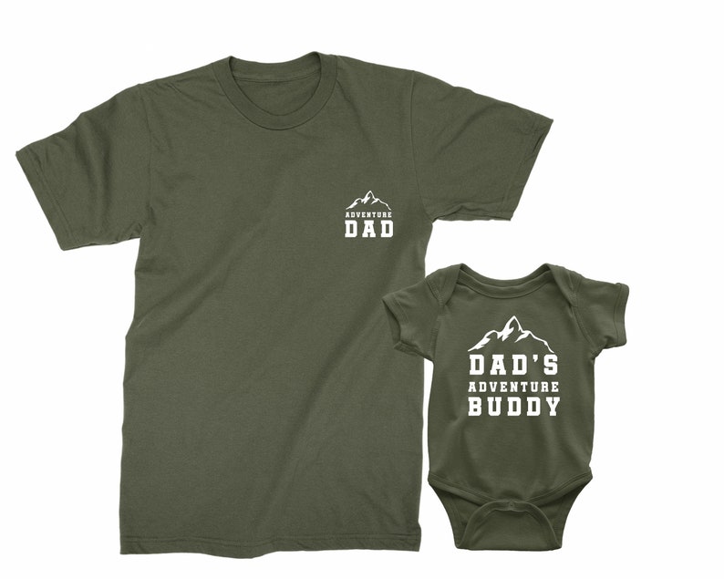 May include: Olive green t-shirt with the text "ADVENTURE DAD" and a matching olive green baby bodysuit with the text "DAD'S ADVENTURE BUDDY". Both garments feature a white mountain graphic.
