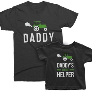 May include: Black t-shirts with a green tractor graphic and text. The larger shirt says "DADDY" and the smaller shirt says "DADDY'S LITTLE HELPER".