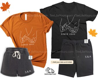 May include: Matching t-shirt and shorts set in burnt orange and black. The t-shirts feature a white line drawing of two hands intertwined, with the text "SINCE 2022". The shorts have initials printed on them.