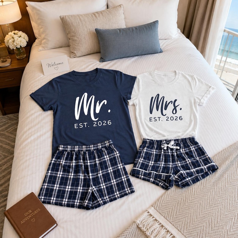 Pu&ograve; includere: Una t-shirt blu navy con testo bianco Mr. EST. 2026 e una t-shirt bianca con testo blu navy Mrs. EST. 2026, abbinate a due paia di pantaloncini a quadri blu navy e bianchi con elastico in vita e coulisse bianca.