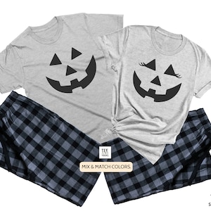 May include: A matching set of two gray t-shirts with a black jack-o'-lantern face design. One shirt has eyelashes on the jack-o'-lantern face. The shirts are paired with black and blue plaid pajama pants. The text "Mix & Match Colors." is printed on a white tag.