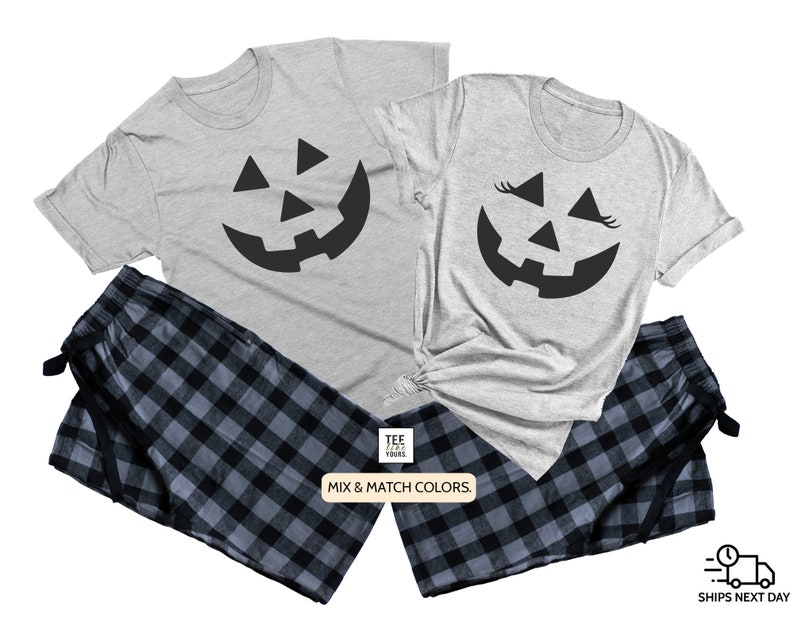 May include: A matching set of two gray t-shirts with a black jack-o'-lantern face design. One shirt has eyelashes on the jack-o'-lantern face. The shirts are paired with black and blue plaid pajama pants. The text "Mix & Match Colors." is printed on a white tag.