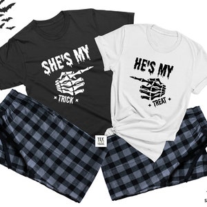 Op de afbeelding: Een bijpassende pyjamaset voor een stel, met een zwart-wit geruit patroon. De shirts hebben een skelet-handgrafiek met de tekst "She's My Trick" en "He's My Treat".