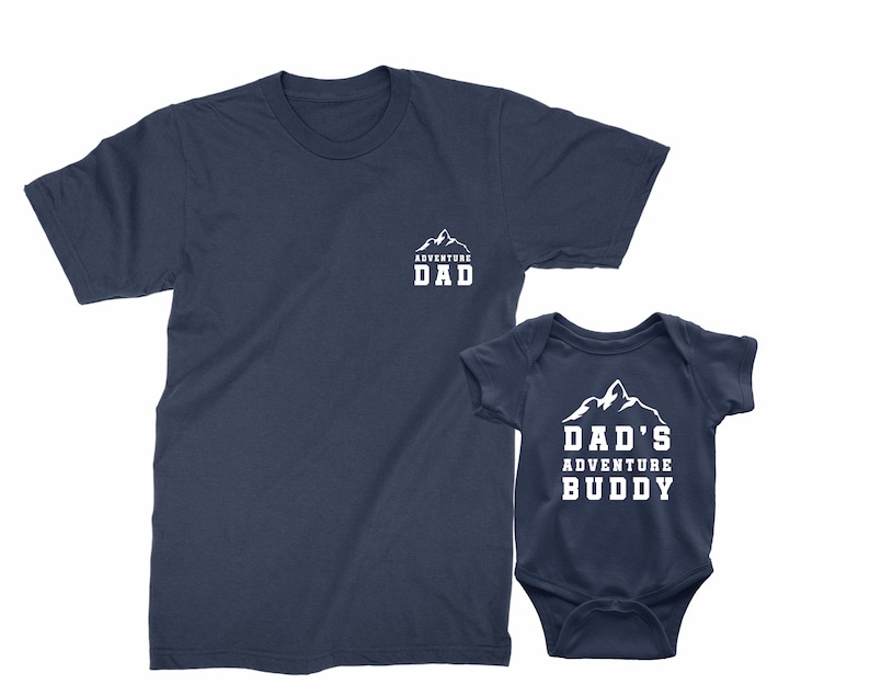 May include: Navy blue t-shirt with the text "ADVENTURE DAD" and a matching navy blue baby bodysuit with the text "DAD'S ADVENTURE BUDDY". Both items feature a white mountain graphic.