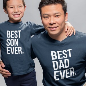 May include: A father and son wearing matching navy blue t-shirts. The father's shirt says "BEST DAD EVER." The son's shirt says "BEST SON EVER."