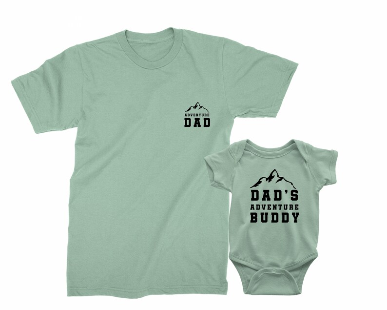 May include: Two matching light green shirts. One is a t-shirt with "ADVENTURE DAD" printed in black. The other is a baby onesie with "DAD'S ADVENTURE BUDDY" printed in black. Both shirts have a mountain graphic.