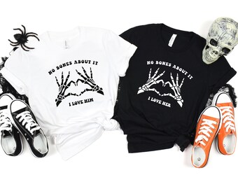 May include: Two t-shirts with a skeleton hand heart design and the text "No bones about it" and "I love him" on one shirt and "I love her" on the other.