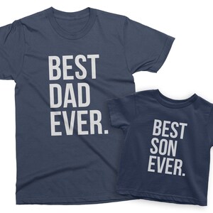 May include: Two navy blue t-shirts with white text. The larger shirt says "Best Dad Ever." The smaller shirt says "Best Son Ever."