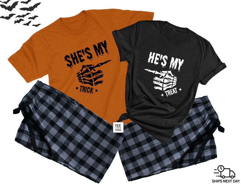 Op de afbeelding: Twee bijpassende T-shirts met een skelet-handmotief en de tekst "She's My Trick" en "He's My Treat". De shirts zijn oranje en zwart en worden gecombineerd met zwart-grijze geruite pyjamabroeken.