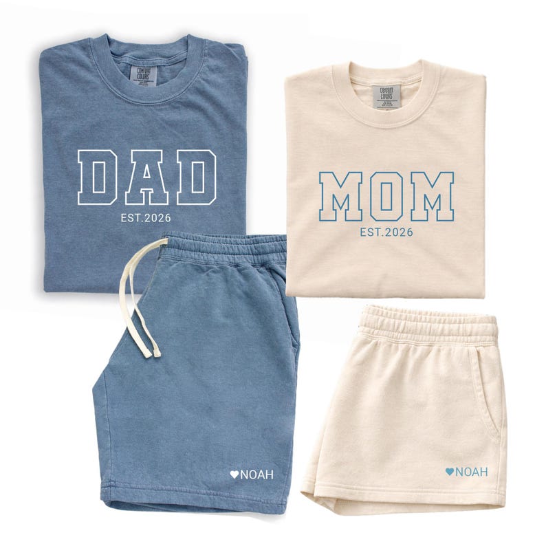 Peut inclure: Deux ensembles assortis de v&ecirc;tements d&eacute;contract&eacute;s. L'un est bleu avec "DAD EST. 2026" sur le t-shirt et le short avec "NOAH" et un c&oelig;ur. L'autre est cr&egrave;me avec "MOM EST. 2026" sur le t-shirt et le short avec "NOAH" et un c&oelig;ur.