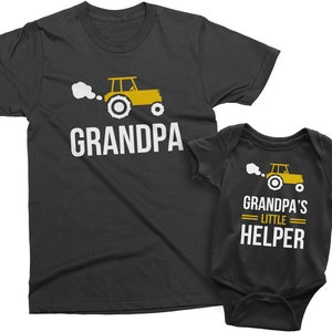 May include: A black t-shirt with the text "GRANDPA" and a yellow tractor with white smoke. A black bodysuit with the text "GRANDPA'S LITTLE HELPER" and a yellow tractor with white smoke.