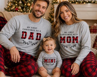 May include: Matching gray long-sleeve shirts and a baby onesie featuring red and black buffalo plaid text. The shirts read My First Christmas As A Dad and My First Christmas As A Mom, while the onesie reads My First Christmas Mini, all with 2026.