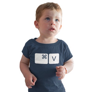 May include: A young child wearing a navy blue t-shirt with a white graphic of the command, "⌘V", printed on the front.