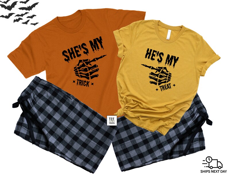 Op de afbeelding: Een bijpassende Halloween pyjamaset voor een stel, met oranje en gele shirts. De shirts hebben een skelethand die wijst met de tekst "She's My Trick" en "He's My Treat". De set bevat zwarte en grijze geruite pyjamabroeken.