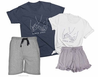 May include: A matching set of two t-shirts with a simple line drawing of two hands holding pinky fingers, with the text "Since 2022" underneath. The t-shirts are in navy blue and white. The set also includes a pair of gray shorts and a pair of gray shorts with ruffles.