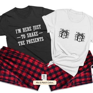 May include: A matching set of two black and white t-shirts with a Christmas theme. One shirt says "I'm here just to shake the presents" and the other shirt has a graphic of two wrapped presents with bows. The shirts are paired with red and black plaid pyjama pants.