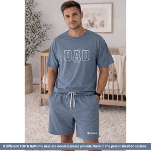 Peut inclure: Un ensemble de pyjama bleu compos&eacute; d'un haut &agrave; manches courtes et d'un short. Le haut affiche le mot "DAD" en lettres blanches avec "EST 2026" en dessous. Le short a un cordon de serrage et le nom "NOAH" avec un c&oelig;ur.