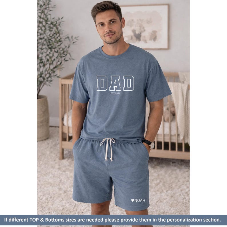Peut inclure: Un ensemble de pyjama bleu compos&eacute; d'un haut &agrave; manches courtes et d'un short. Le haut affiche le mot "DAD" en lettres blanches avec "EST 2026" en dessous. Le short a un cordon de serrage et le nom "NOAH" avec un c&oelig;ur.