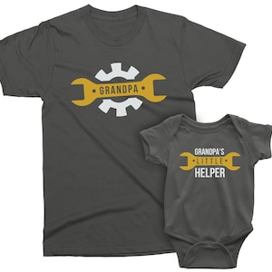May include: A dark gray t-shirt with a white wrench and gear design that says "Grandpa". A matching dark gray baby onesie with a white wrench and gear design that says "Grandpa's Little Helper".