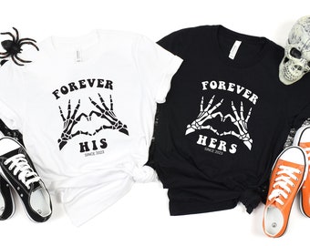 May include: Two black and white t-shirts with a skeleton hand heart design. The white shirt says "Forever His Since 2023" and the black shirt says "Forever Hers Since 2023".